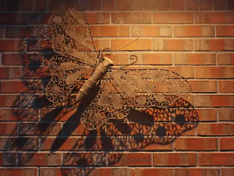 Metal butterfly art casting a large shadow on a brick wall
