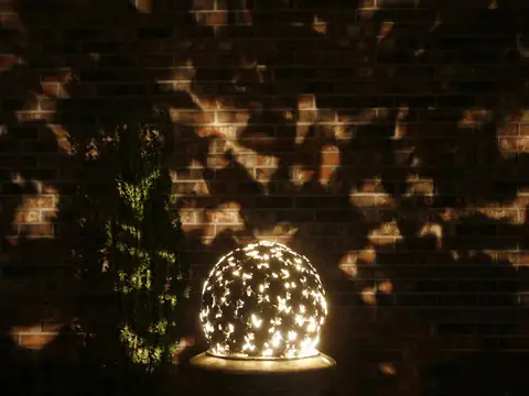 Pierced sphere sculpture lit from within, throwing a pattern of light across the brick wall behind it