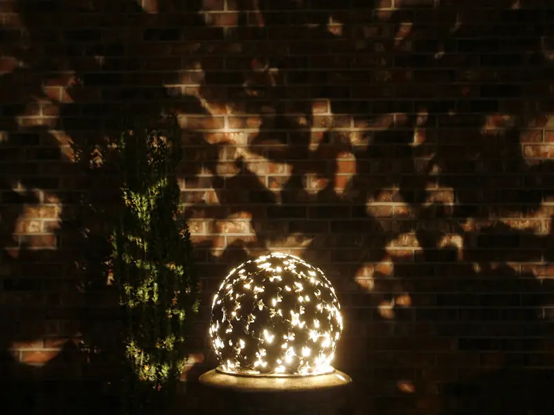 Pierced sphere sculpture lit from within, casting a pattern of light across a brick wall behind it