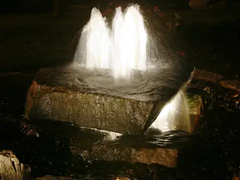 Bubbling rock water feature lit from beneath at night with the surrounding stone and planting dark