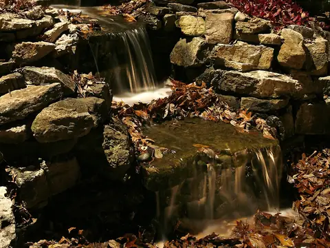 Stone waterfall over rock ledges at night with autumn planting lit alongside