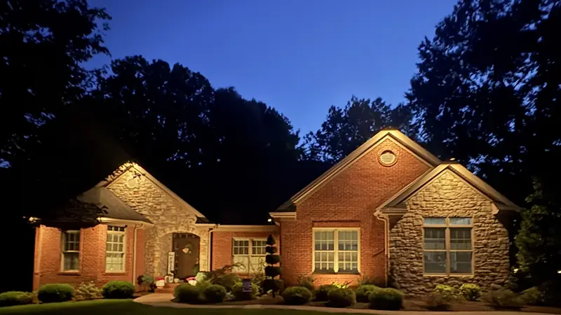 The same brick and stone house with its gables grazed from below and the front beds lit