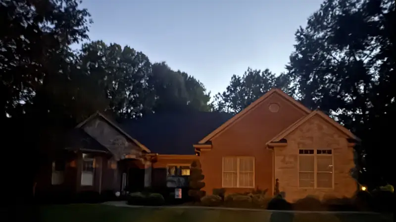 Brick and stone ranch house at dusk with its landscape lighting off, the walls going dark