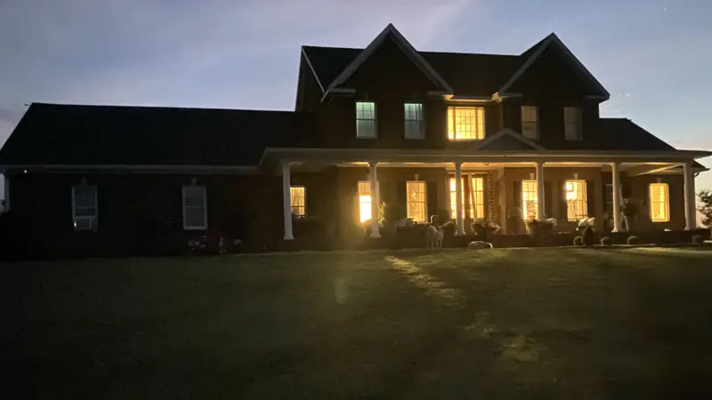 Two-story brick house with a long front porch at dusk, lighting off, lit only by its windows