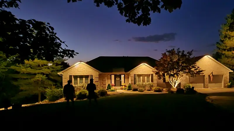 The same ranch house with each gable washed from its peak and the tree by the drive uplit