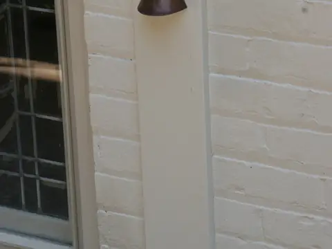 A small conical fixture mounted high under a soffit, photographed in daylight against pale siding