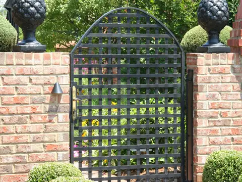 Brick garden wall and ornamental iron gate in daylight with dark fixtures against the piers