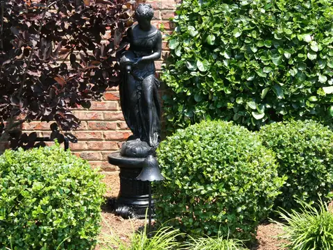 Garden statue on a plinth surrounded by clipped shrubs in daylight, the fixture hidden in the planting