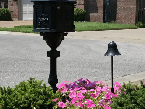 Black path light and a lamp post beside a driveway photographed in daylight