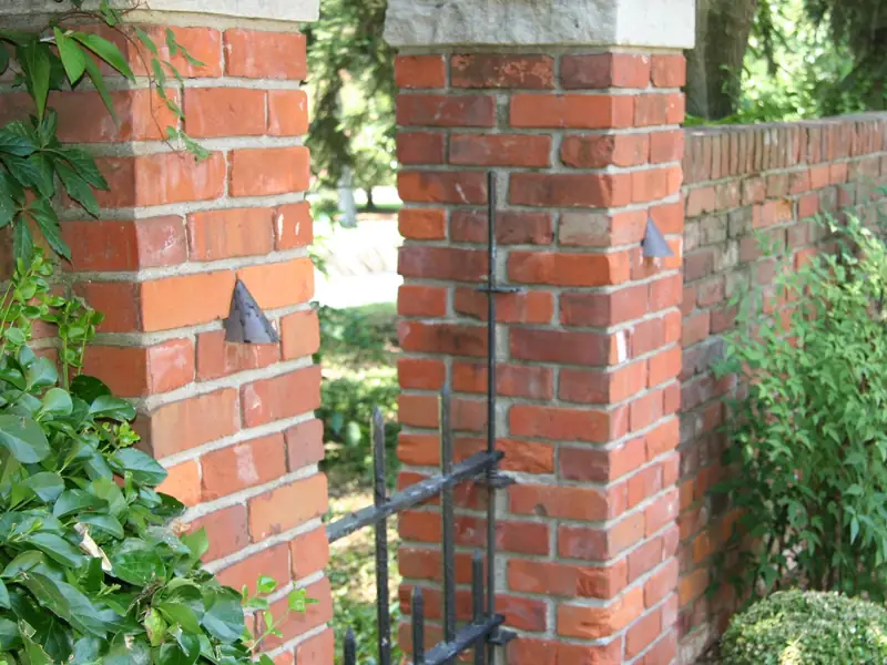 Brick pillar photographed in daylight with a small dark fixture mounted against the mortar and no visible cable
