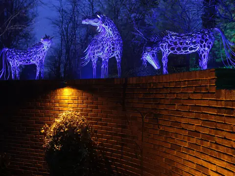 Wire horse sculptures lit blue above a warm-washed brick wall