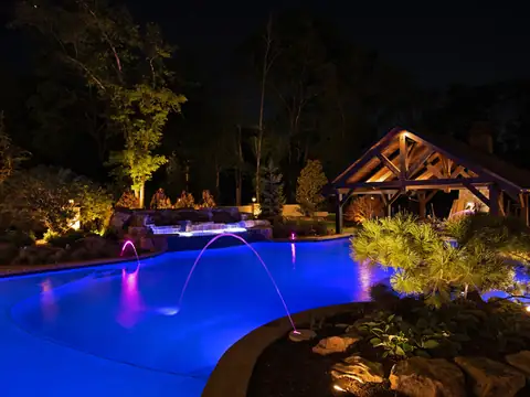 Blue-lit pool with magenta water jets and a timber pavilion beyond