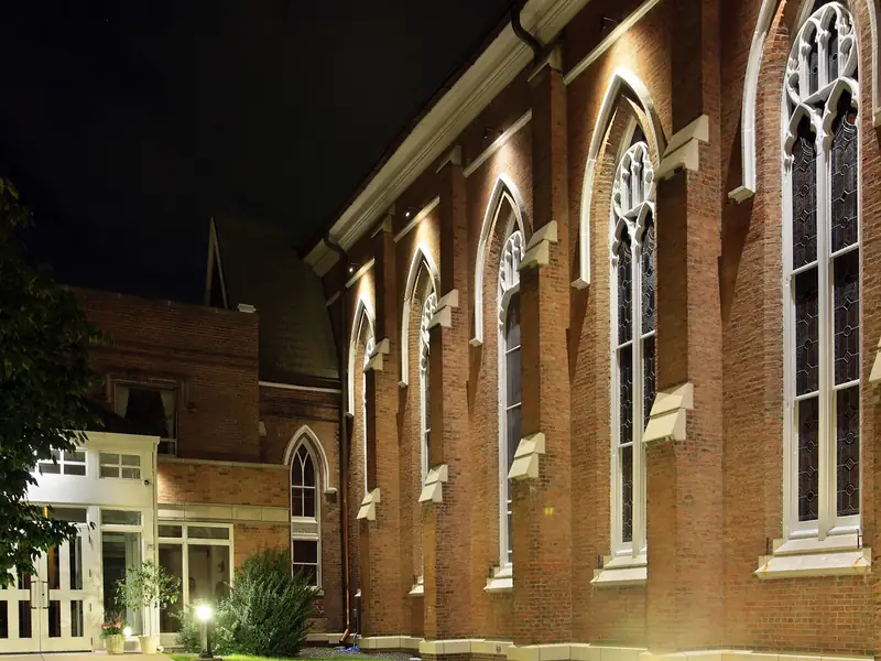 Brick church elevation at night with tall arched windows grazed by warm light from ground level