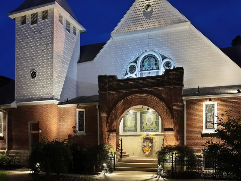 Brick church with a white bell tower and arched entry lit at dusk against a deep blue sky