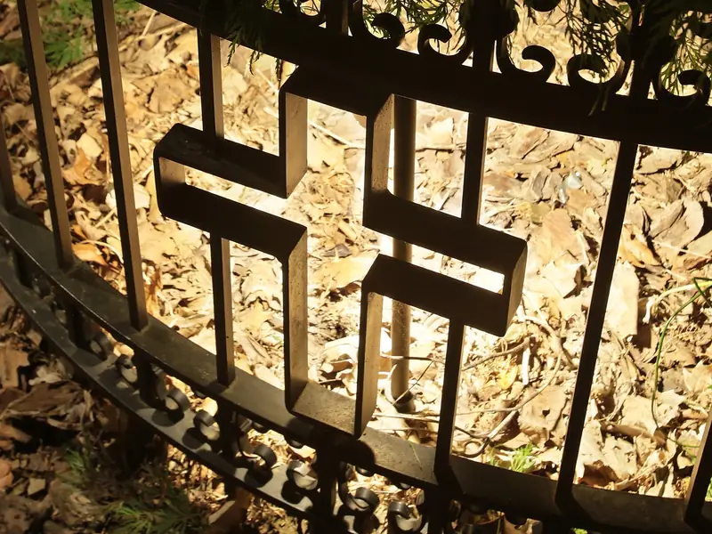 Ornamental ironwork panel lit at night from behind, the pattern silhouetted against the lit surface beyond