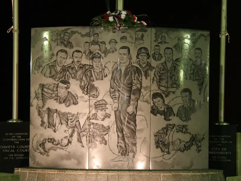 Etched glass memorial panel lit from below at night, the engraved figures and lettering clearly legible