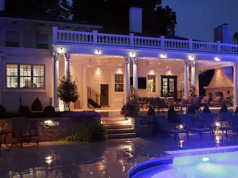White columned house above a lit pool at night with the terrace and steps lit from the sides