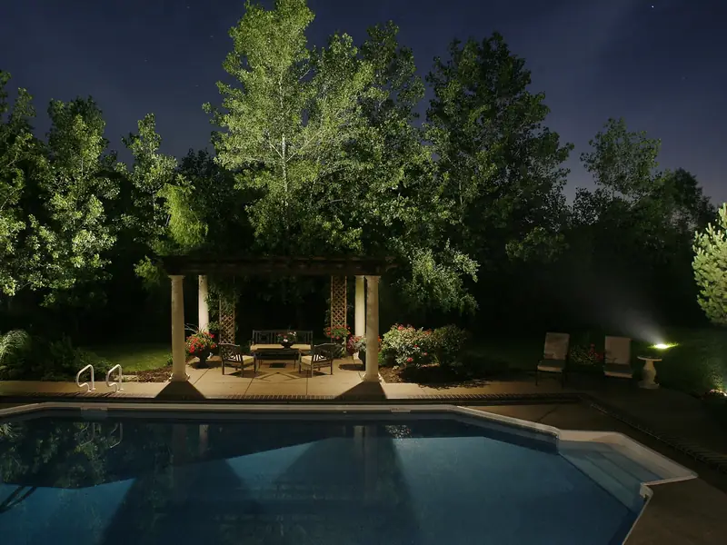Pool and pavilion at night with the surrounding tree line lit softly from within the canopy