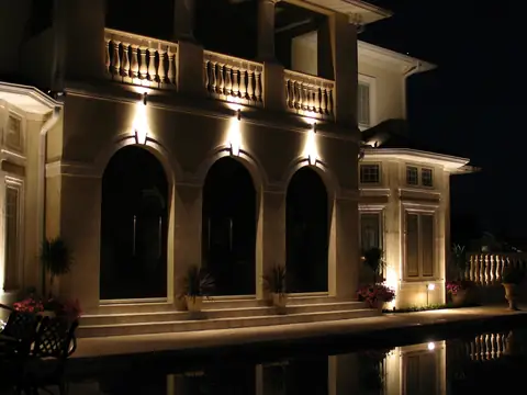 Arched stucco elevation at night with downlights under each arch and a pool in the foreground