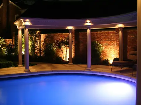 Curved pool at night beside a brick colonnade with the columns washed in warm light