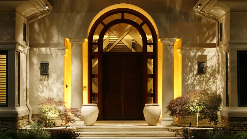 Arched wooden entry door lit from concealed fixtures set into the surrounding stone archway