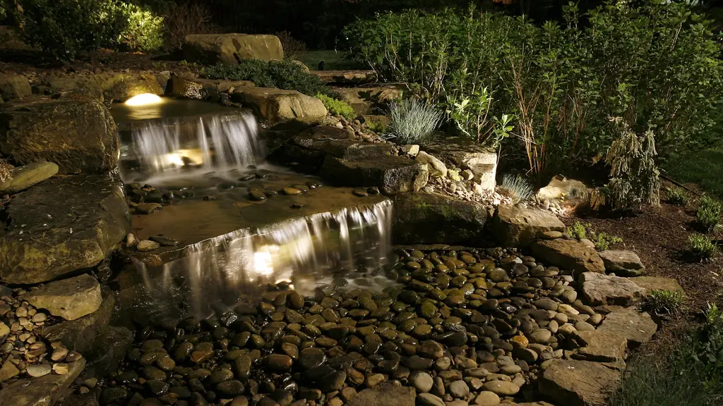 Stone waterfall and stream lit from within so the moving water glows against the dark planting