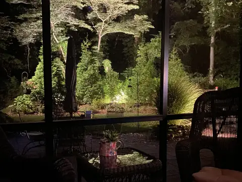 Screened porch at night looking out on uplit trees and plantings