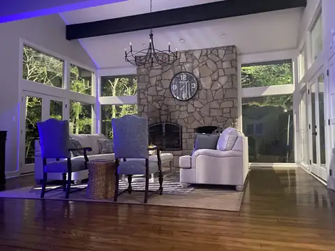 Sunroom with a stone fireplace at night, lit trees in every window