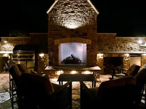Outdoor kitchen and stone fireplace at night with the chimney face lit from below