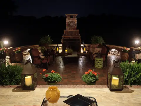 Brick patio and outdoor fireplace at night with lanterns and lit planters