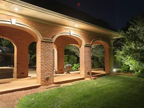 Arched brick loggia with downlights in its ceiling above a lawn
