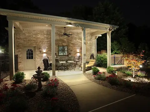Covered pavilion at the end of a lit walk, with garden accents and an uplit ornamental tree