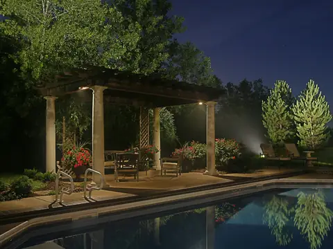 Pergola and pool at night with the surrounding trees lit from within the canopy