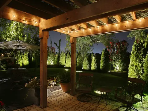 Timber pergola lit from the beams with planting and a garden path visible beyond