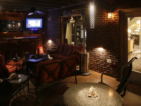 Covered outdoor bar and seating area with brick walls, lit warmly with a fire bowl on the table