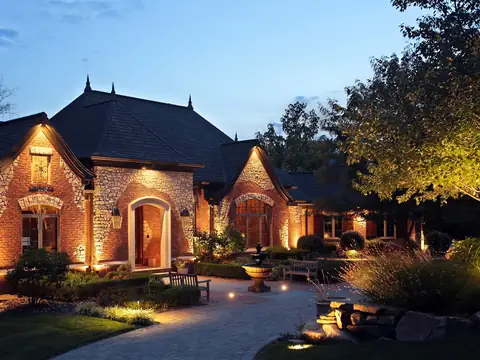 Stone house and circular drive at blue hour, gables uplit and the motor court lit from the tree canopy