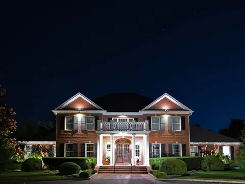 Brick colonial with lit columns, balcony and gables at night