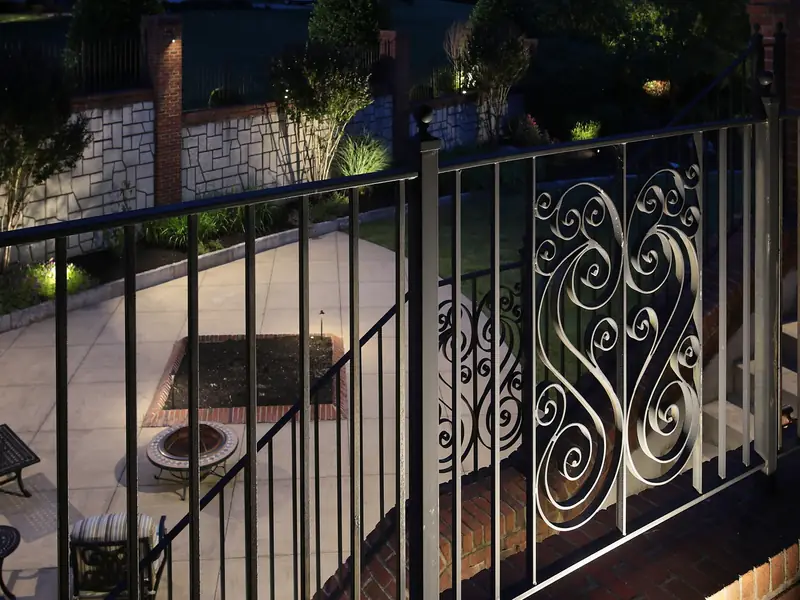 Ornamental iron railing and stone steps lit from below at night with the patio beyond softly lit