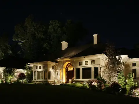 Long low house at night with the entrance portico brightest and the elevation washed evenly to either side