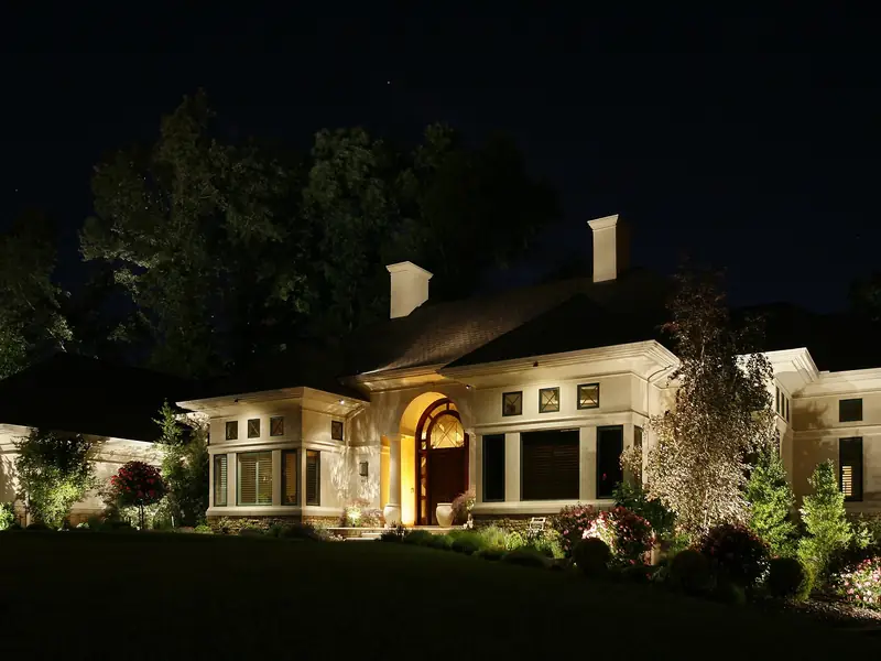 Long low house at night with a lit entrance portico and evenly washed elevation running away to both sides
