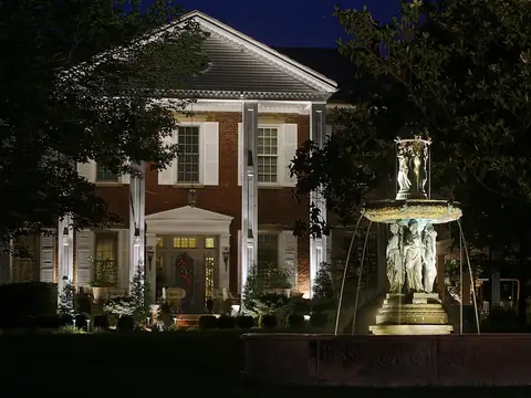 Symmetrical white columned house at night with a lit stone fountain in the foreground