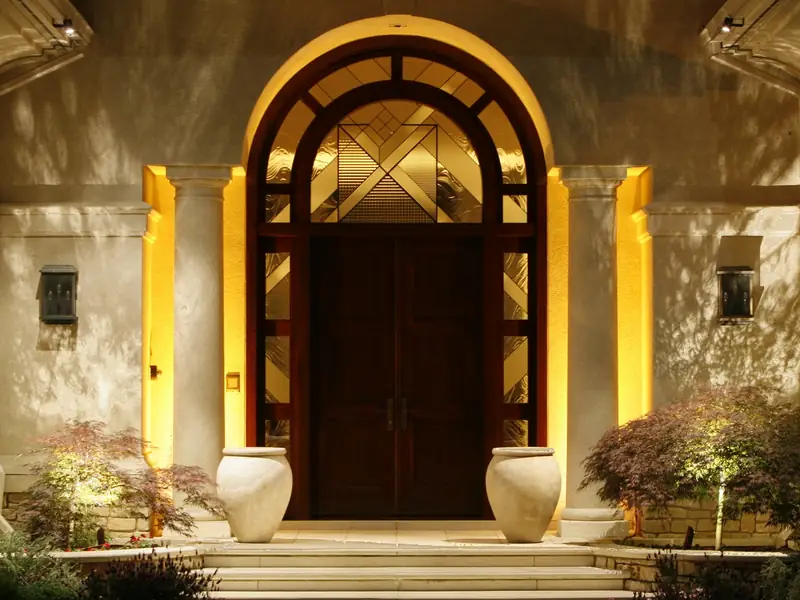 Arched wooden front door lit from concealed fixtures in the surrounding stone archway