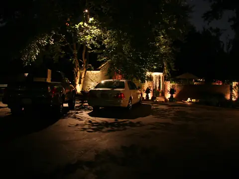 Parking court at night beside a house, lit from the surrounding trees rather than from poles