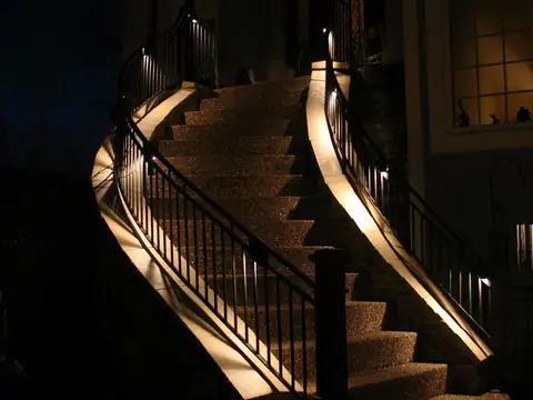 Curving exterior staircase and iron handrail lit from beneath so each tread edge is visible