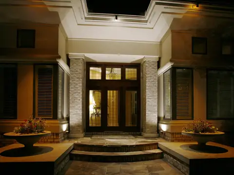 Front entrance with stone steps and planters lit evenly at night, the doorway clearly legible